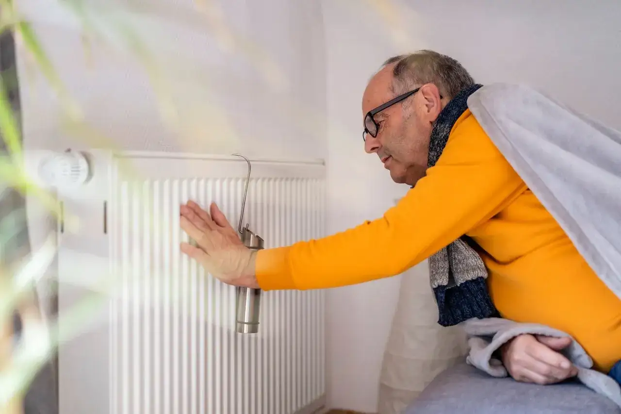 Mann pr&uuml;ft Heizung. Kein warmwasser und heizung wie lange zumutbar? Er ist in Decken geh&uuml;llt.