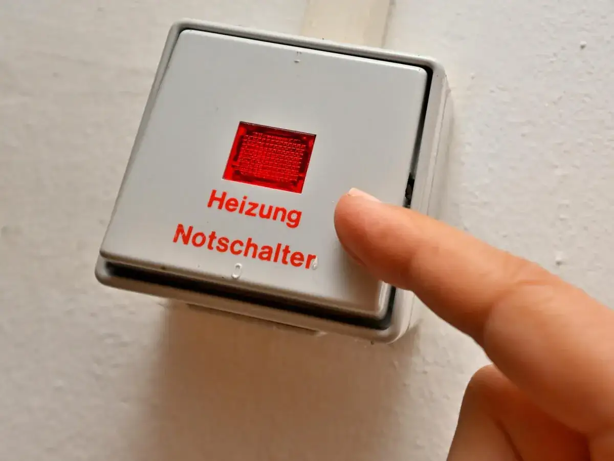 Ein Finger drückt auf den roten Heizungs-Notschalter. Dieser Schalter ist in vielen Gebäuden Pflicht, um im Notfall die Heizung schnell abschalten zu können.