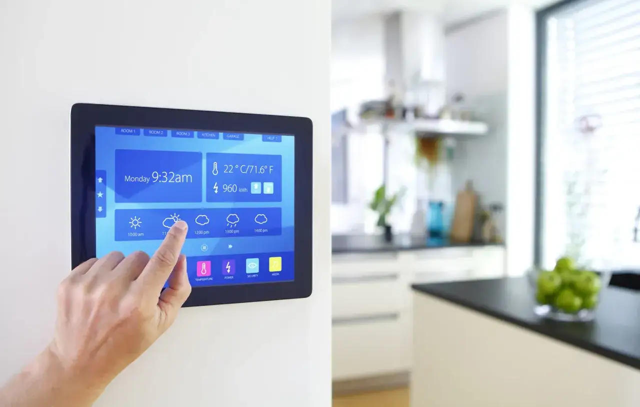 Ein Finger tippt auf ein Tablet, das das Wetter und die Energieanzeige eines smarten Zuhauses zeigt. Die Küche ist unscharf im Hintergrund zu sehen.