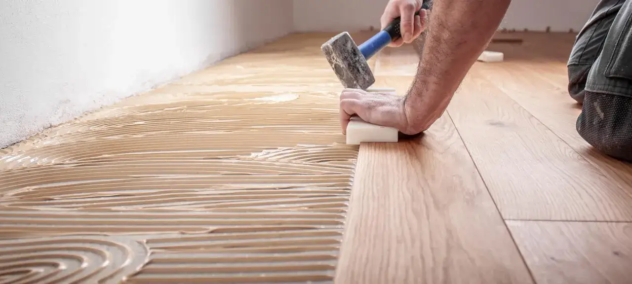 Hand verlegt Holzparkett mit Kleber. Die sorgfältige Arbeit beim Linoleum verlegen sorgt für ein schönes Ergebnis.