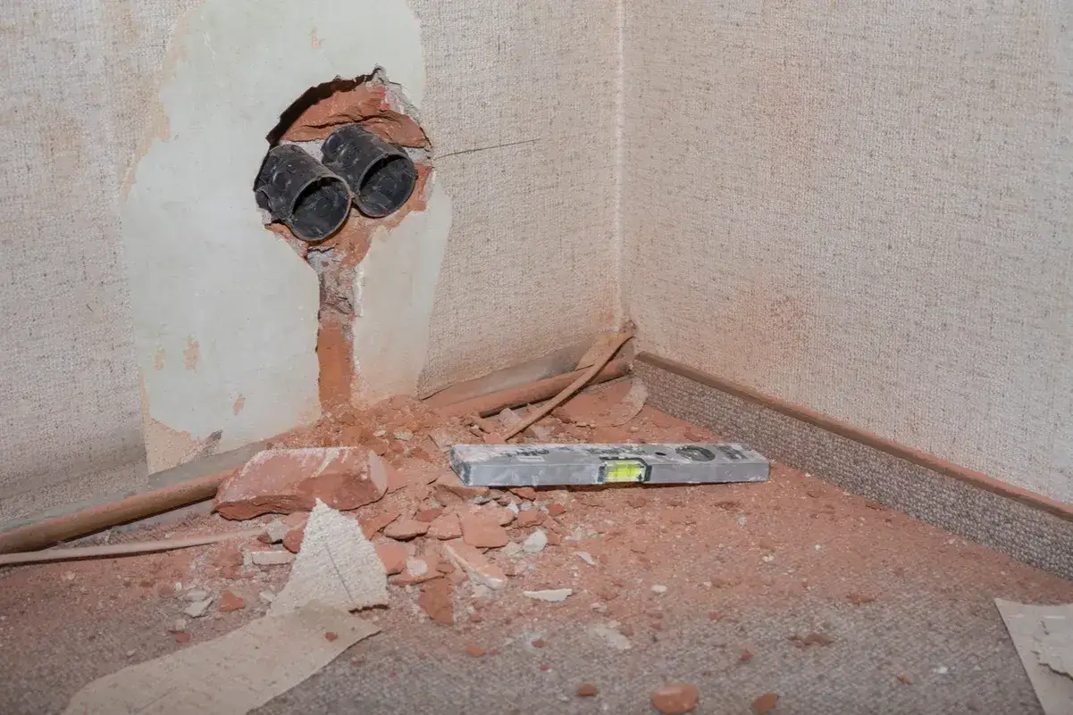 Baustelle in der Wohnung: Aufgebrochene Wand mit Rohren, Ziegelsteinen und Wasserwaage. Grund für Mietminderung.