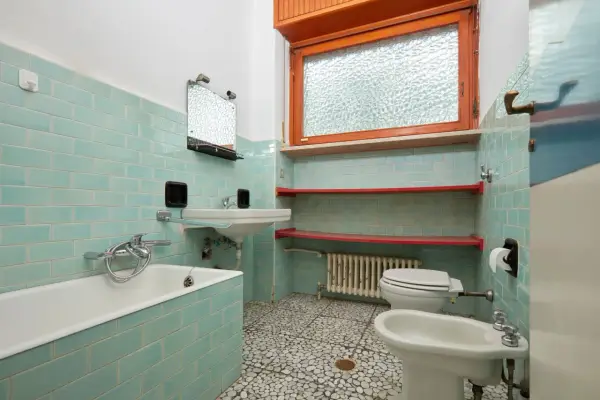 Altes Bad mit türkisen Fliesen, Wanne, Waschbecken, Toilette und Bidet. Hier stellt sich die Frage, wann muss Vermieter Bad renovieren?