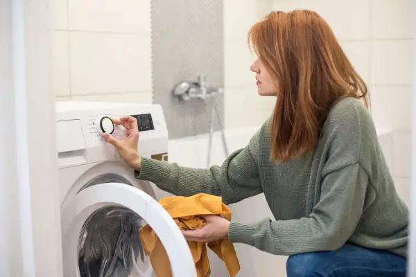 Frau stellt Waschmaschine ein, achtet auf wasserverbrauch. Sie hält ein gelbes Kleidungsstück.