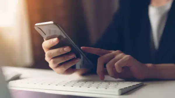 Person tippt auf Smartphone, weil hey Google funktioniert nicht. Tastatur und Maus im Vordergrund.